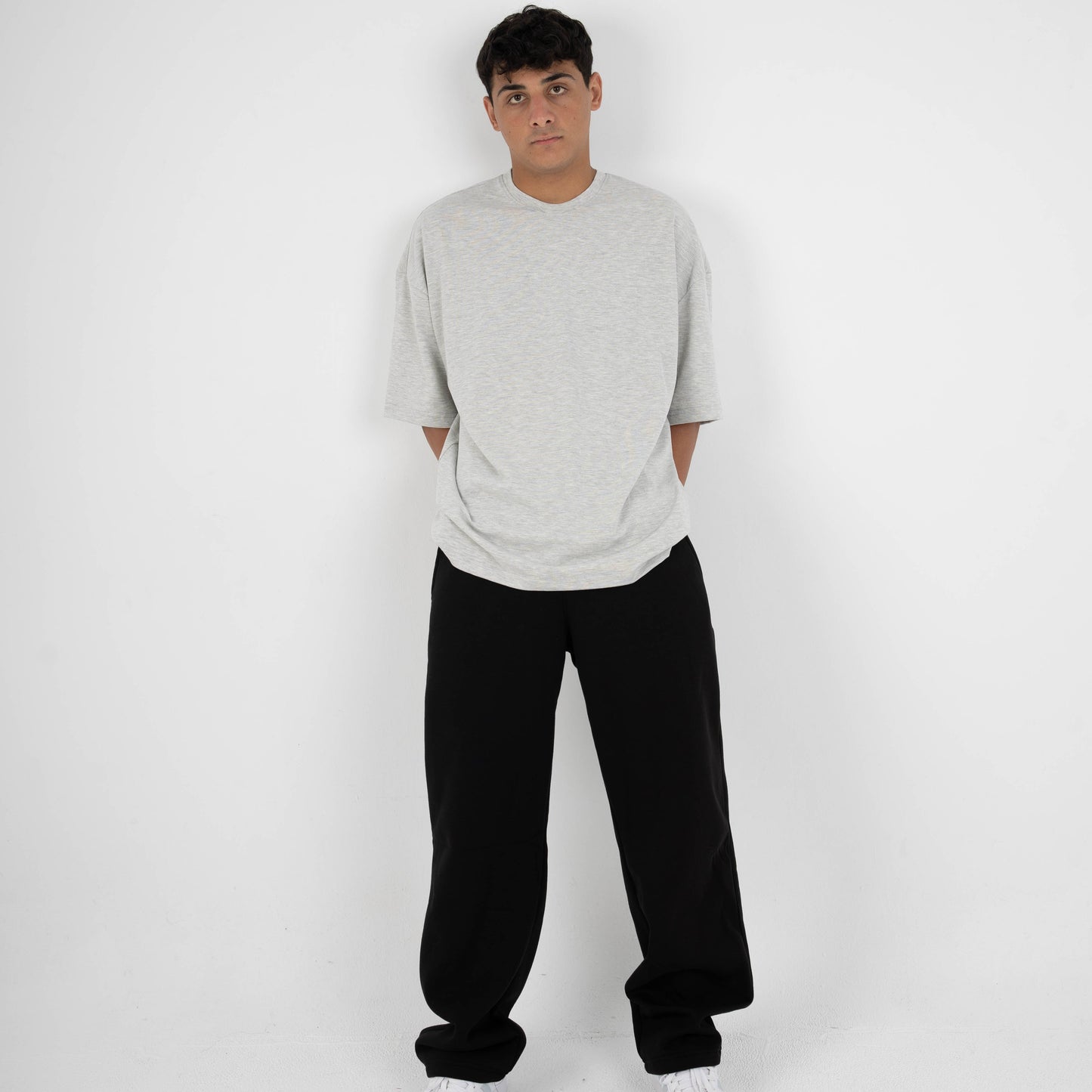 Person wearing a gray sweater, black pants, and white shoes on a white background
