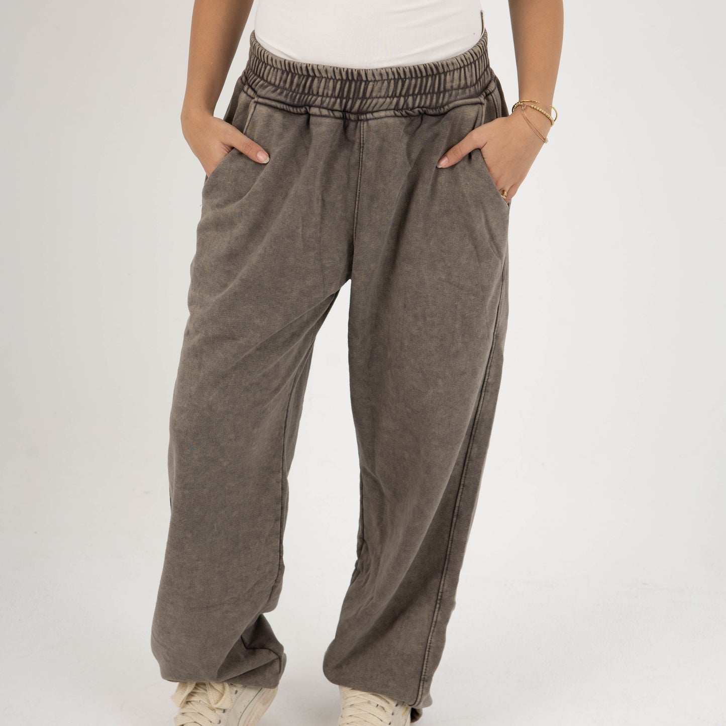 Person wearing brown wide-leg pants and a white top on a plain background