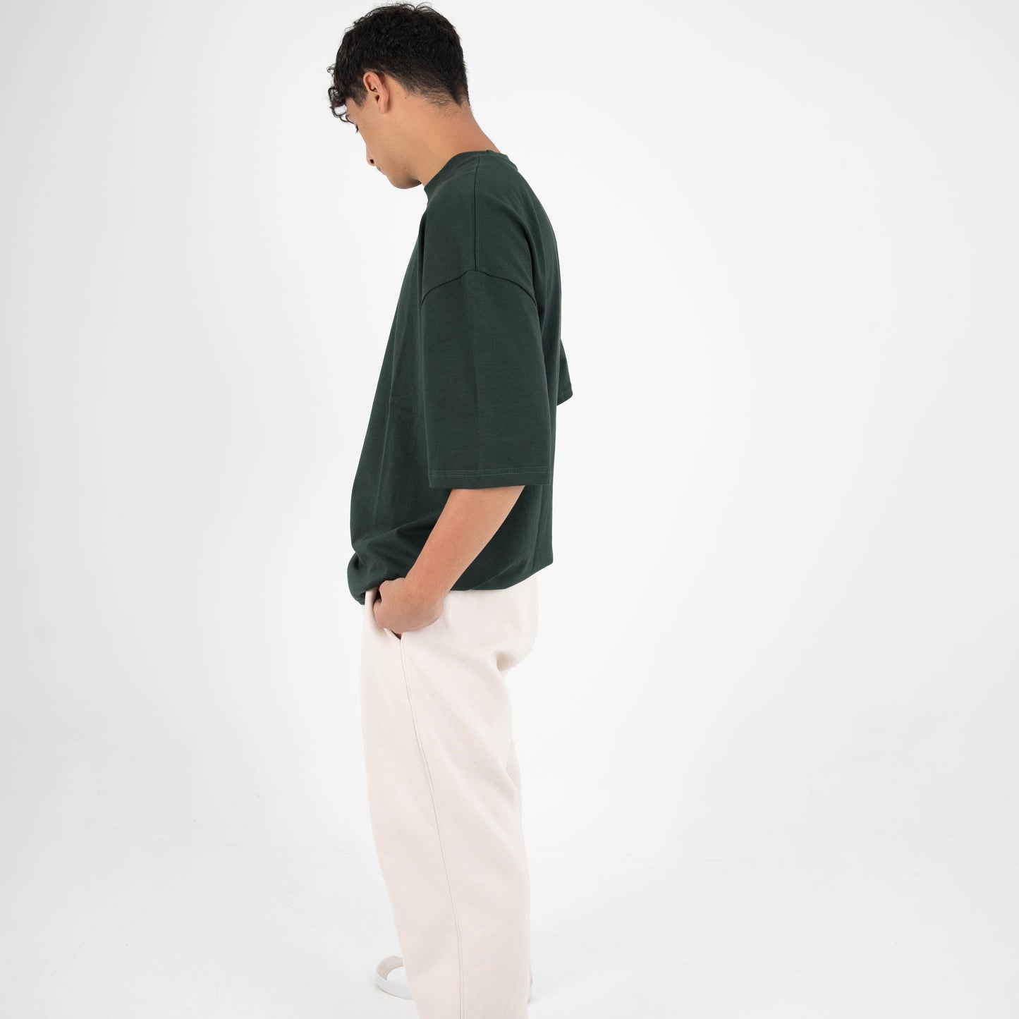 Person wearing a dark green shirt and light-colored pants on a white background