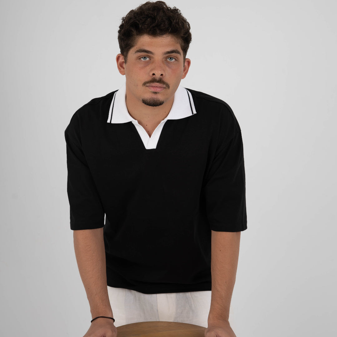 Man wearing a black sweater with white collar holding a wooden stool against a plain background