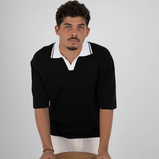 Man wearing a black sweater with white collar holding a wooden stool against a plain background