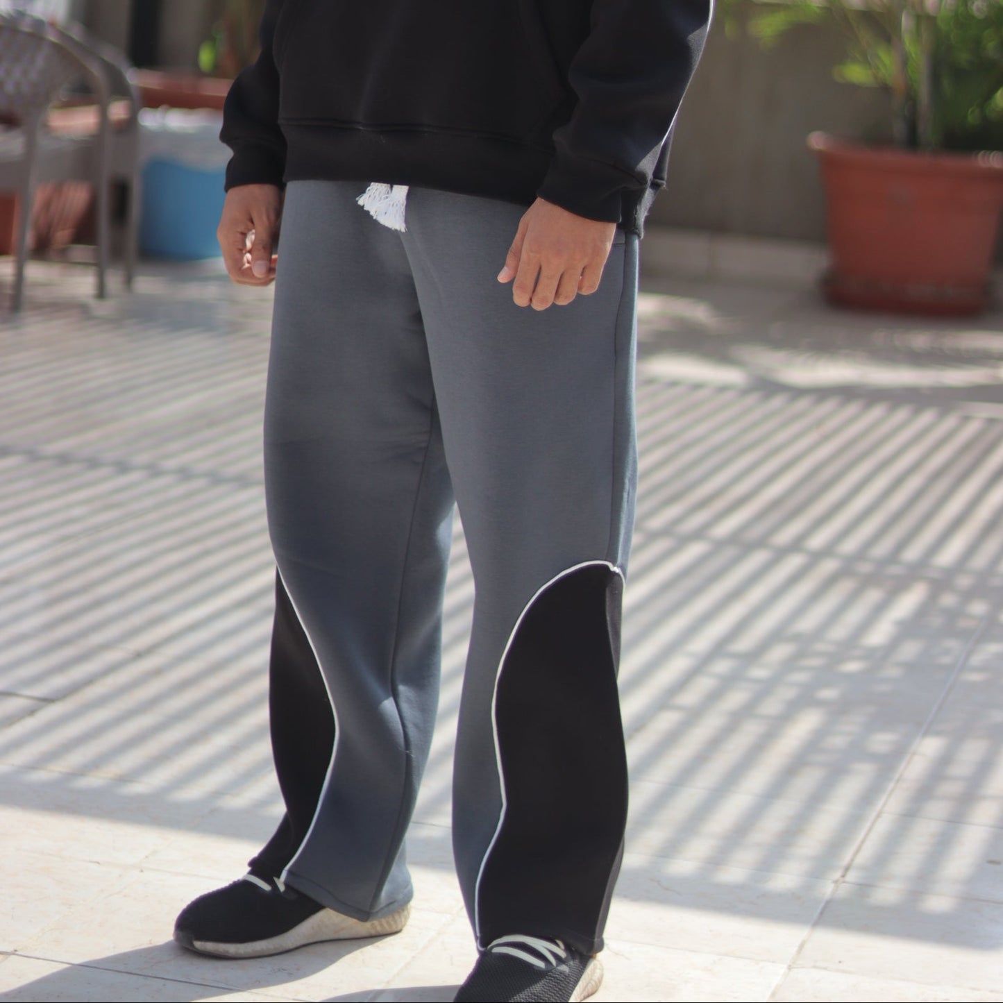 Person wearing a black hoodie with text and gray pants in an outdoor setting.