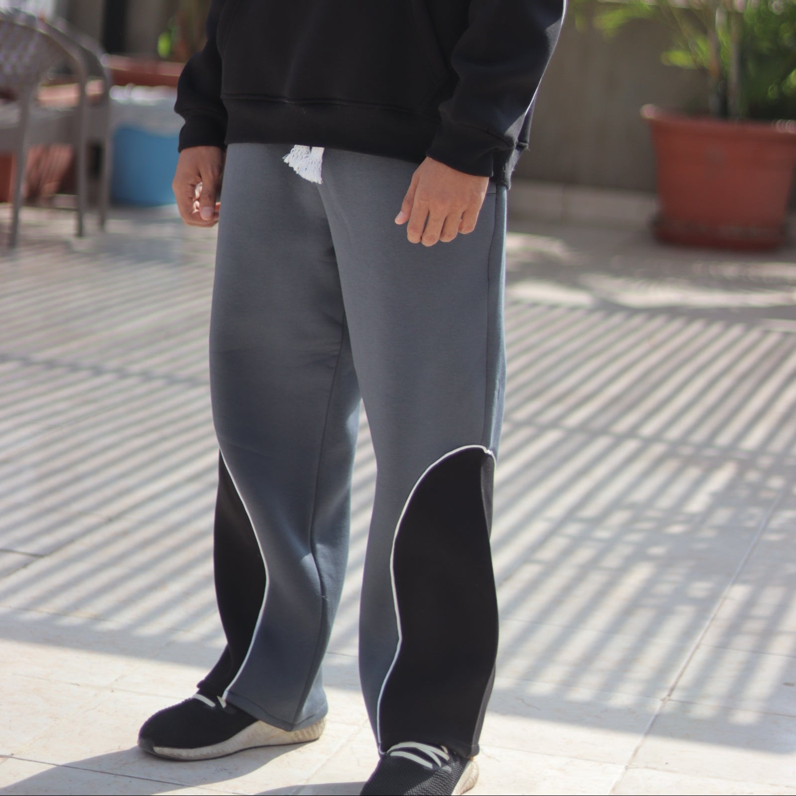 Person wearing a black hoodie with text and gray pants in an outdoor setting.