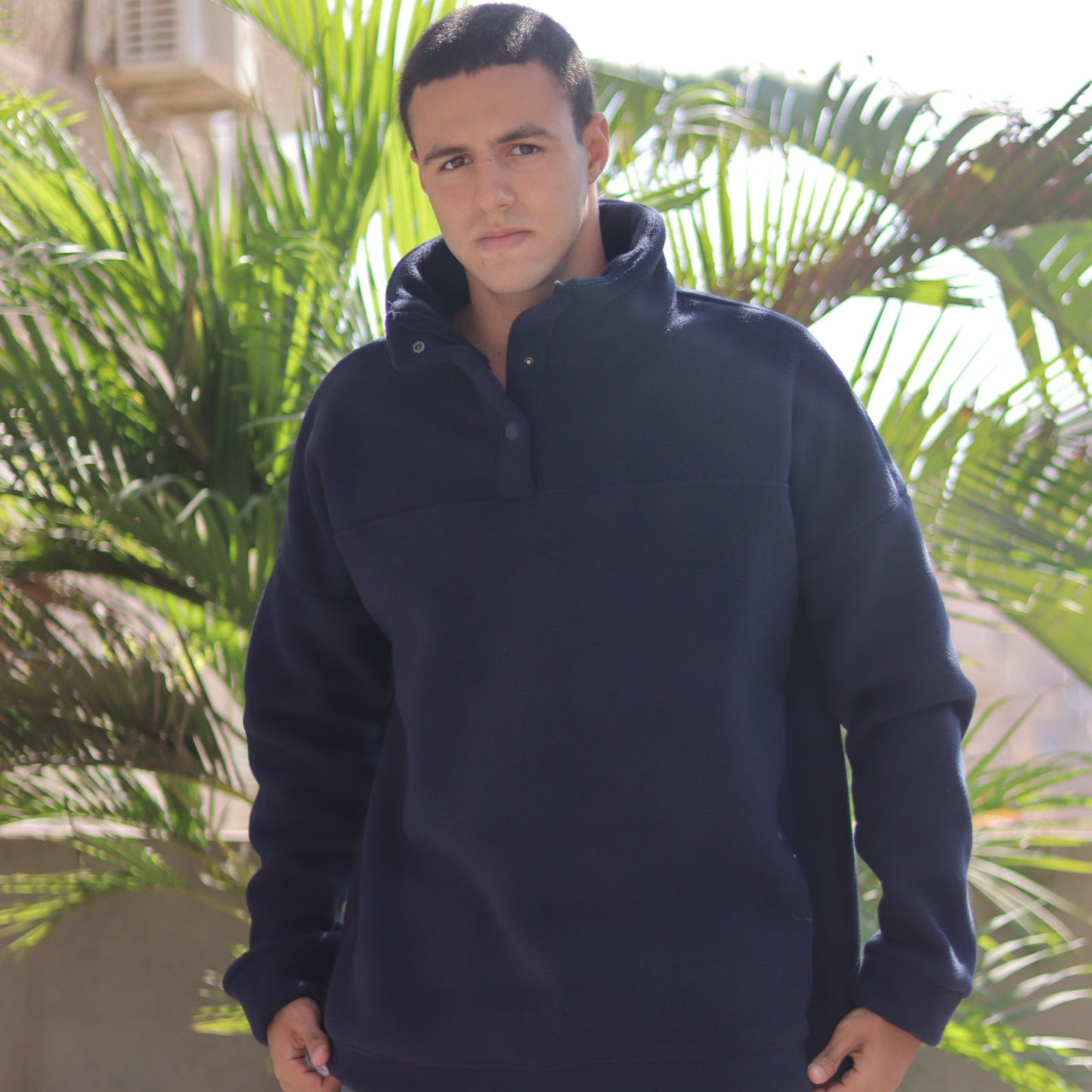 Person wearing a dark blue jacket standing outdoors with greenery in the background